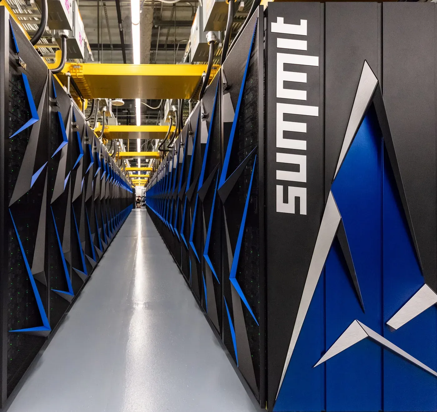 A long aisle between tall black server cabinets with angular blue accent panels, cables running along an overhead yellow gantry, with the word 'Summit' printed vertically on the nearest cabinet.