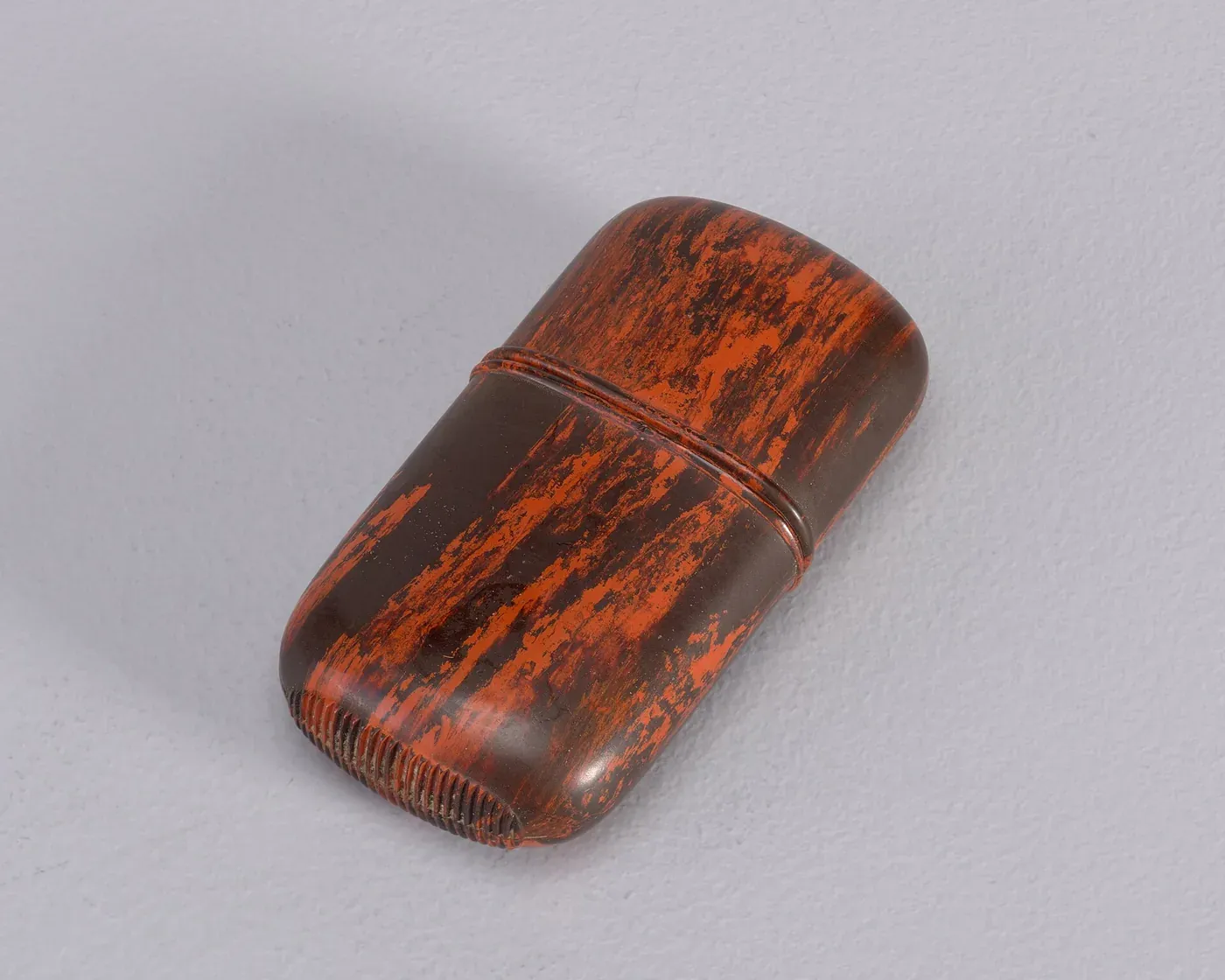 An oblong pocket matchsafe with a slip-top lid, its surface patterned with irregular red and black mottling.