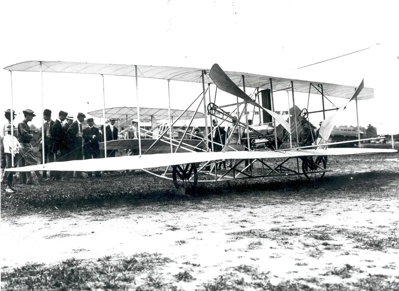 A Wright Flyer biplane standing on grass, a crowd of soldiers and officials gathered along one wing.