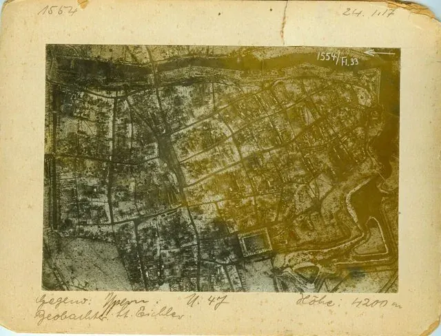 A grainy aerial reconnaissance photograph of a war-damaged town, its streets and building outlines visible from directly above, with handwritten annotations in the margins.