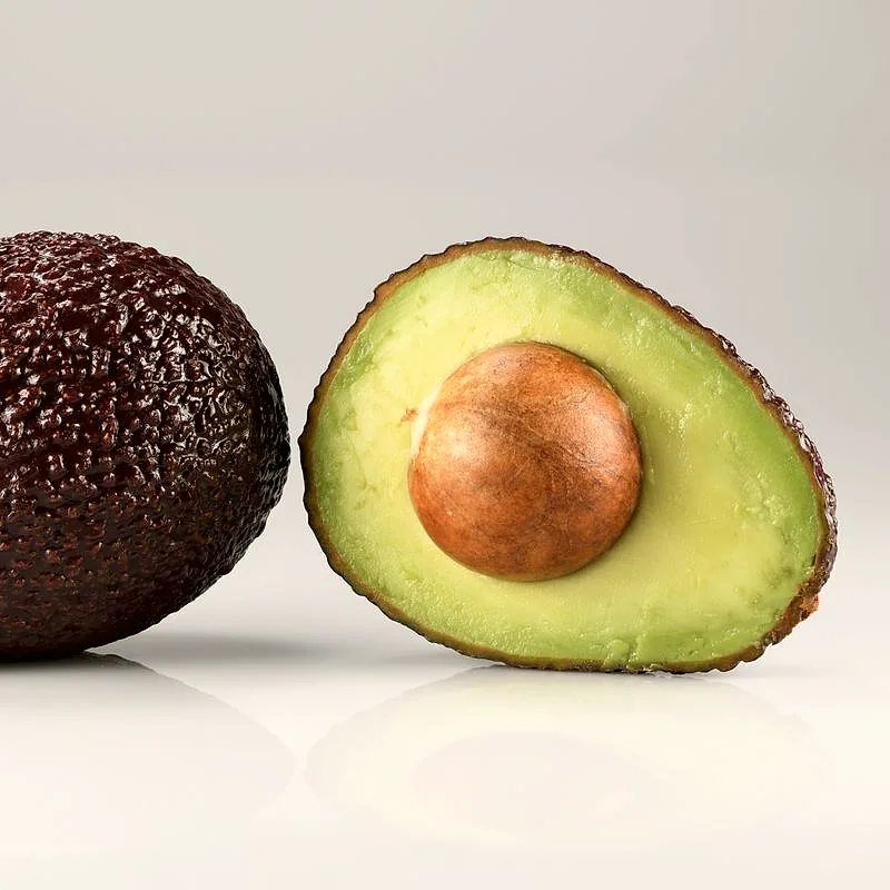 A whole dark-skinned avocado beside one halved around its stone