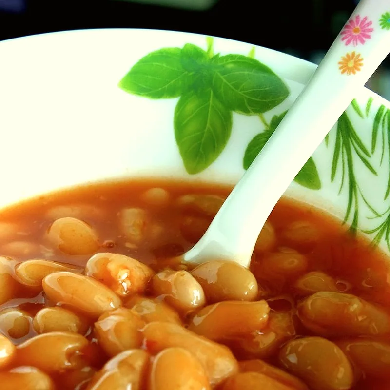 A bowl of baked beans in orange tomato sauce, with a spoon