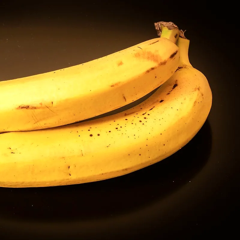 Two ripe yellow bananas with brown speckles, against a dark background
