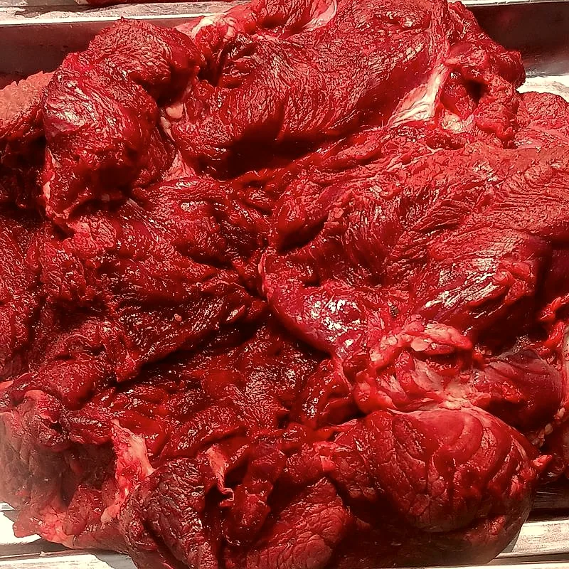 A raw, untrimmed beef brisket at a butcher's counter, showing its deep red marbled muscle