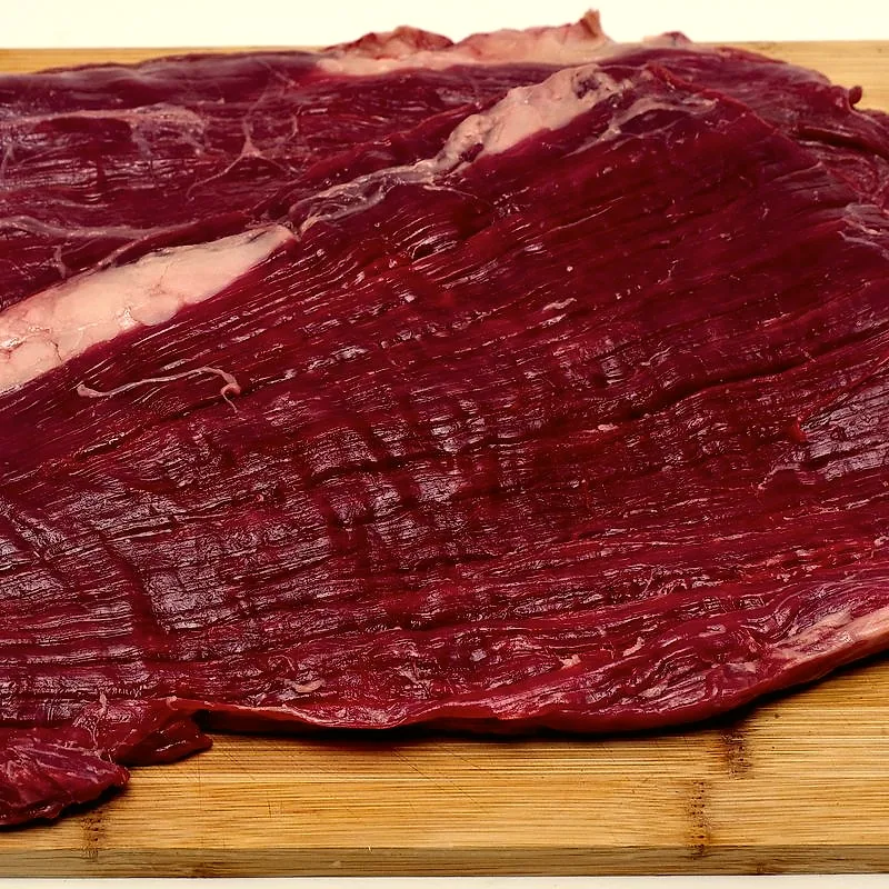 A raw flank steak on a wooden board, showing its long muscle grain and a thin strip of fat