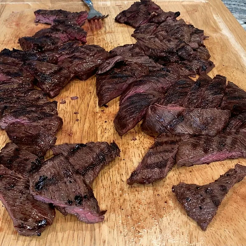 Grilled skirt steak sliced on a wooden board, showing its long muscle grain