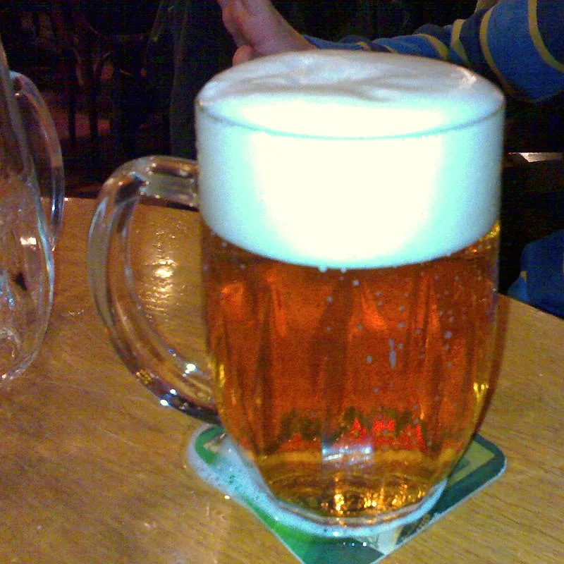 A large mug of pale lager beer with a thick foam head