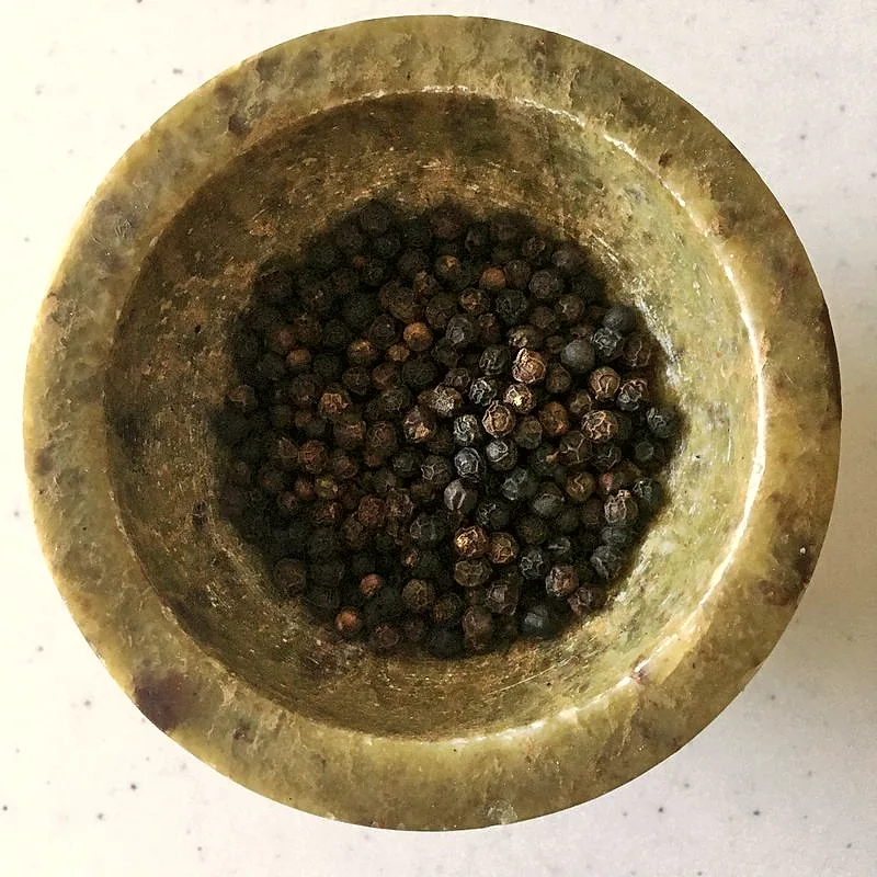 Whole black peppercorns gathered in a brass mortar