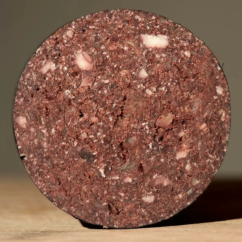 A round cross-section slice of black pudding, dark and dense with visible flecks of fat