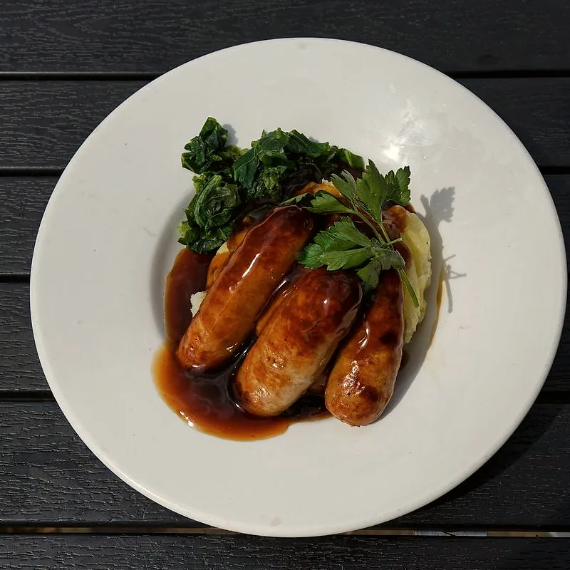 Three plump British pork sausages, browned and glazed with onion gravy, on mashed potato