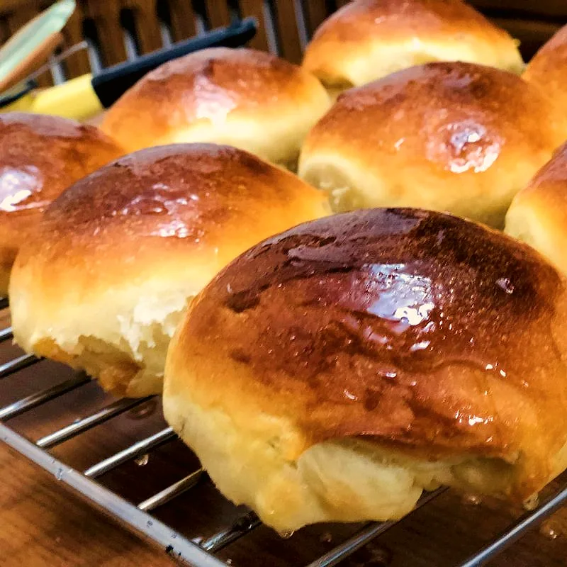Several soft, round burger buns with glossy golden-brown tops, cooling on a wire rack