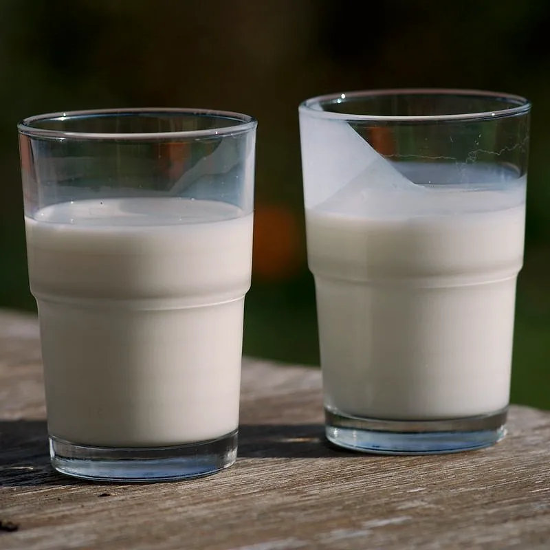 Two glasses of dairy on a wooden table, buttermilk on the right showing a thicker, slightly separated texture next to plain milk