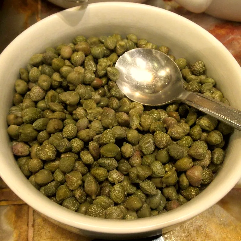 A bowl of small green pickled capers with a spoon