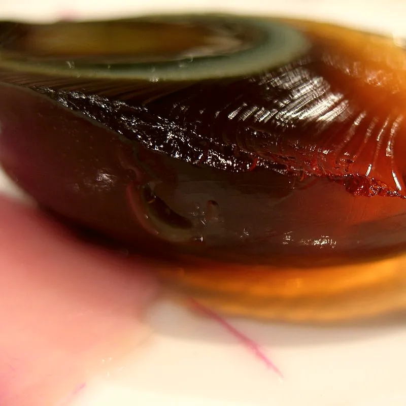 A close-up cross-section of a century egg, showing the dark amber translucent jelly-like white with a crackled pattern around the yolk