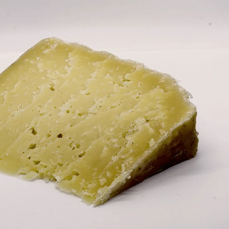 A wedge of crumbly, pale yellow cheddar cheese