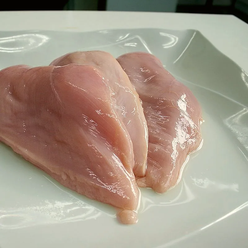 Two raw, boneless chicken breast fillets on a white plate
