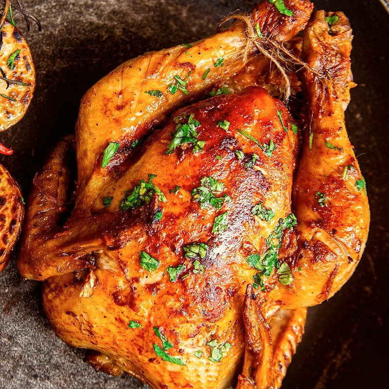 A whole roasted chicken, browned and garnished with chopped herbs