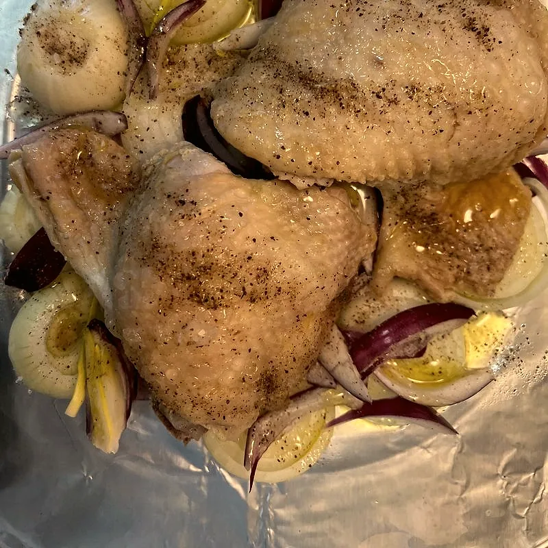 Raw, skin-on chicken thighs seasoned with pepper, resting on sliced onion