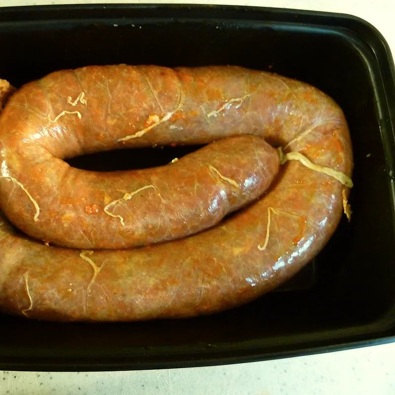 A coiled raw chorizo sausage in its casing, red-orange from paprika