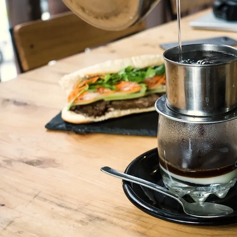 A glass of Vietnamese iced coffee with a visible pooled layer of thick white condensed milk at the bottom