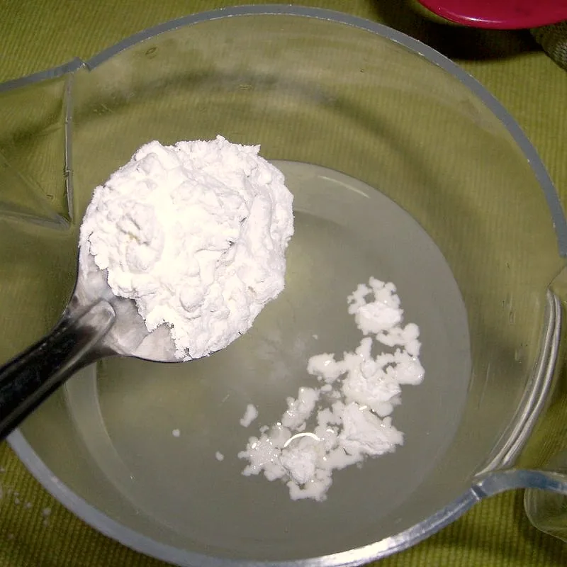 A spoonful of white cornflour being added to water