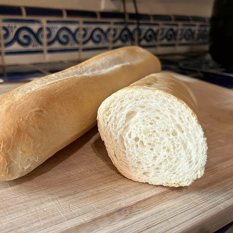 A loaf of Cuban bread cut in half, showing a thin golden crust and soft, airy white crumb