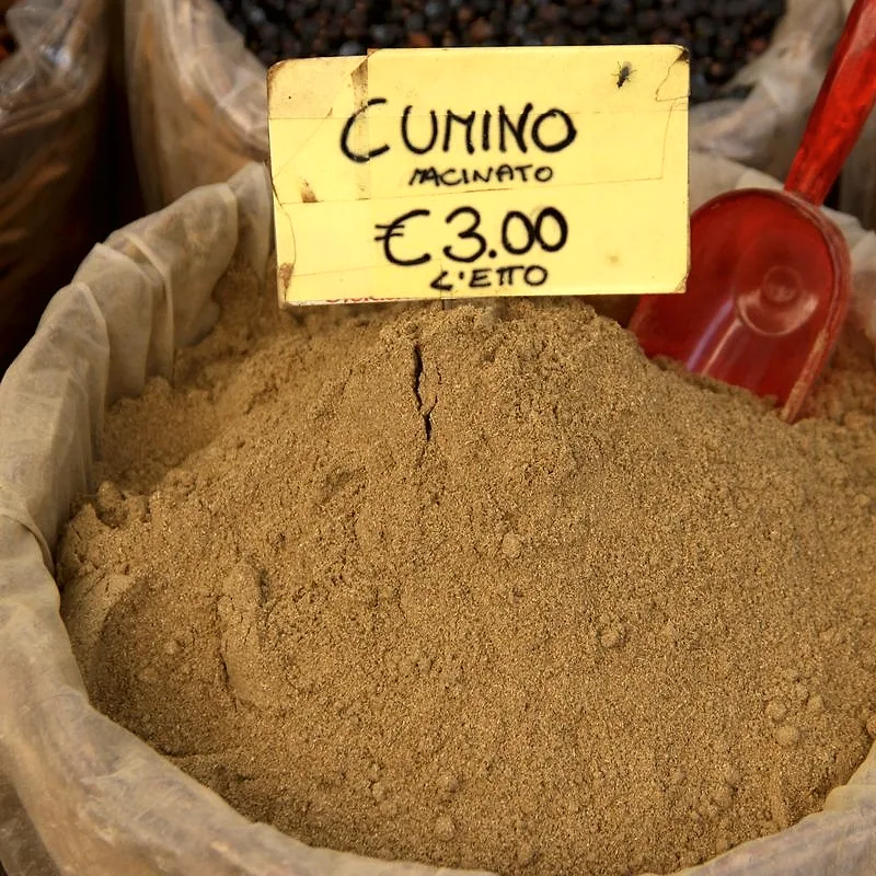 An open sack of ground cumin at a market stall, fine and pale brown