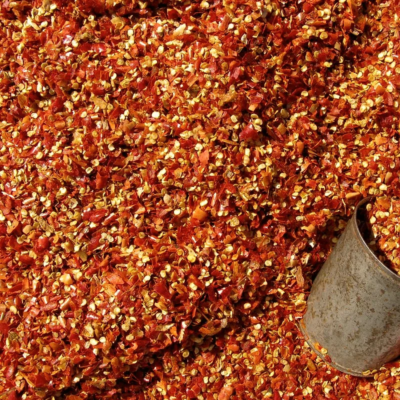 Coarsely ground dried red chilli flakes with their seeds, and a metal scoop