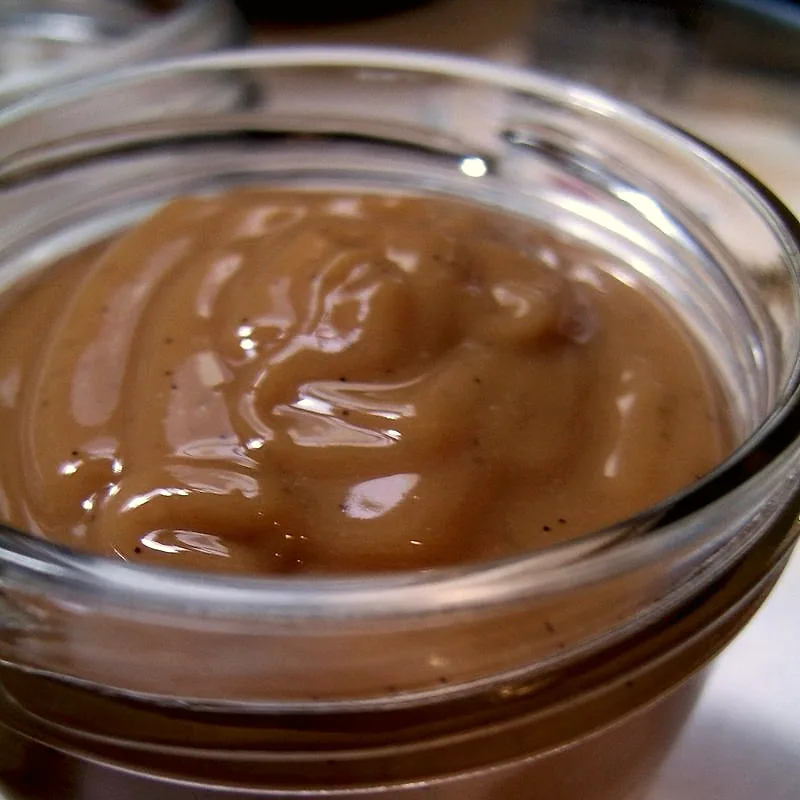 A close-up of smooth caramel-brown dulce de leche in a glass jar
