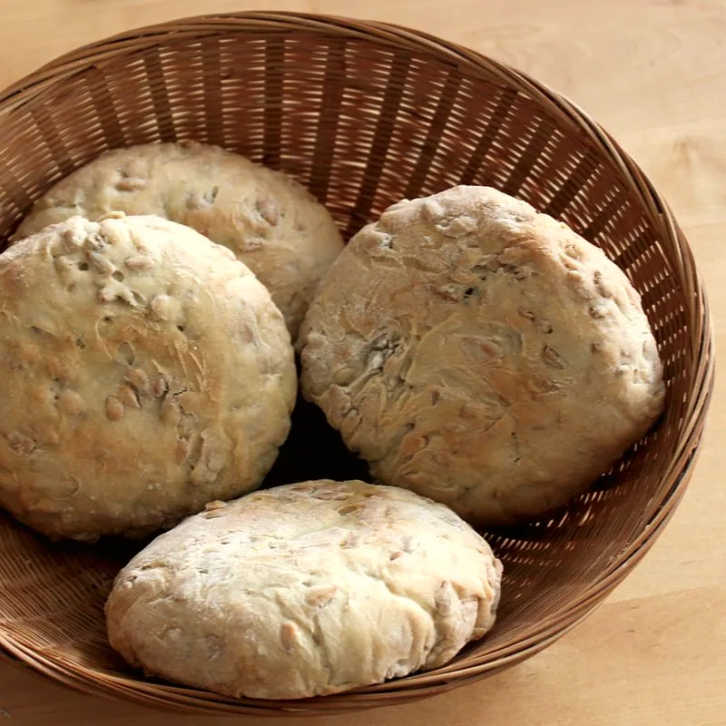 Four whole English muffins with craggy, floury tops piled in a wicker basket