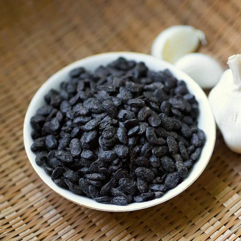 A bowl of dark, wrinkled fermented black beans (douchi), with garlic cloves beside it