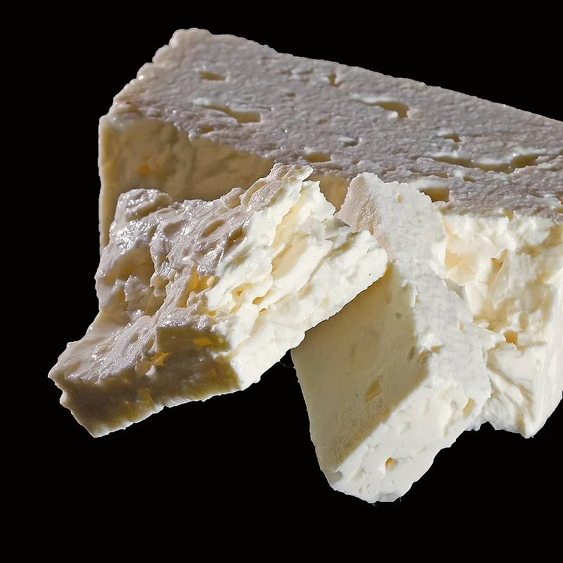 A block of feta cheese with a piece broken off, showing its crumbly white texture