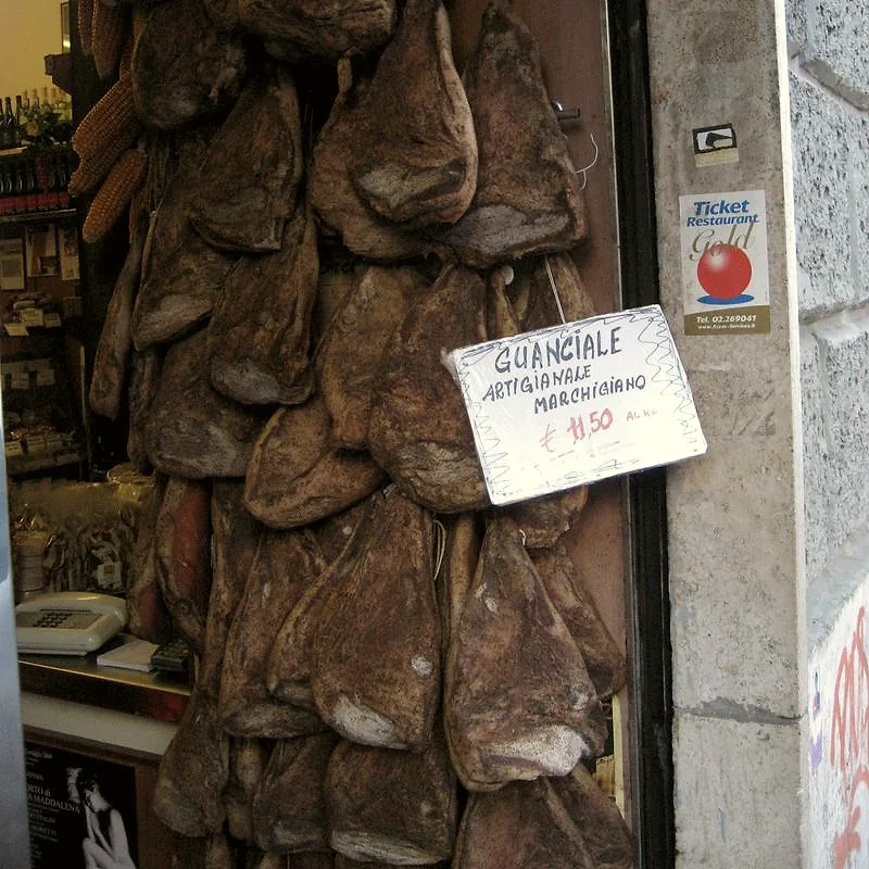 Whole cured guanciale hanging in a shop doorway, dark and dry-rinded