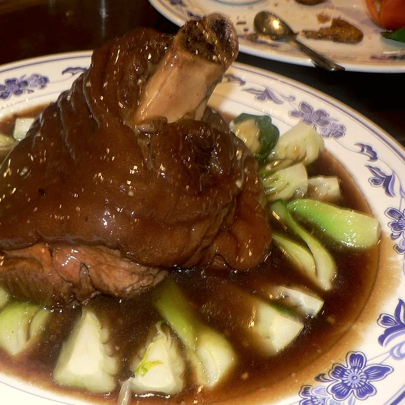 A whole braised pork ham hock in a dark sauce, bone exposed