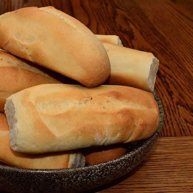 A pile of fresh, golden-crusted hoagie rolls in a bowl