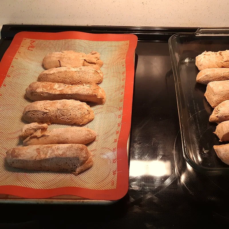 Freshly baked, oblong hot dog buns cooling on baking trays