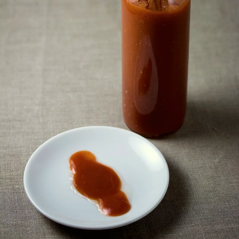 A small pool of red hot sauce on a white plate next to a bottle