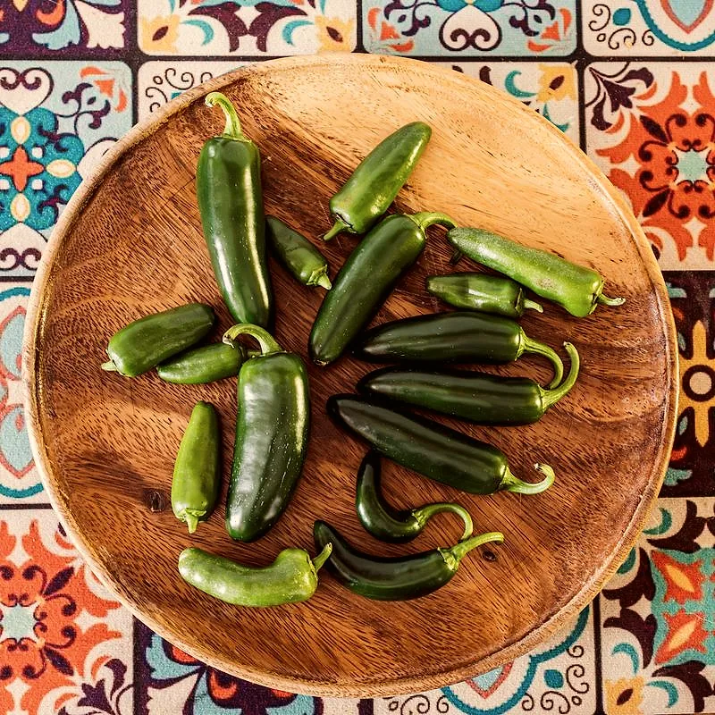 A pile of fresh green jalapeno peppers on a wooden plate