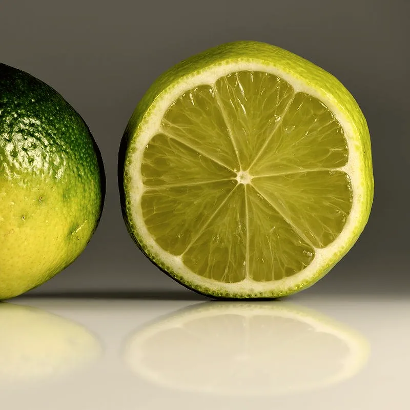 A whole lime beside one cut in half, showing the pale green flesh