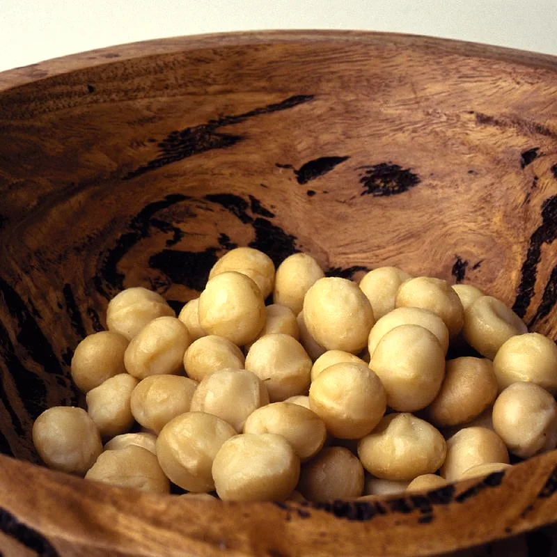 Shelled macadamia nuts piled in a dark wooden bowl