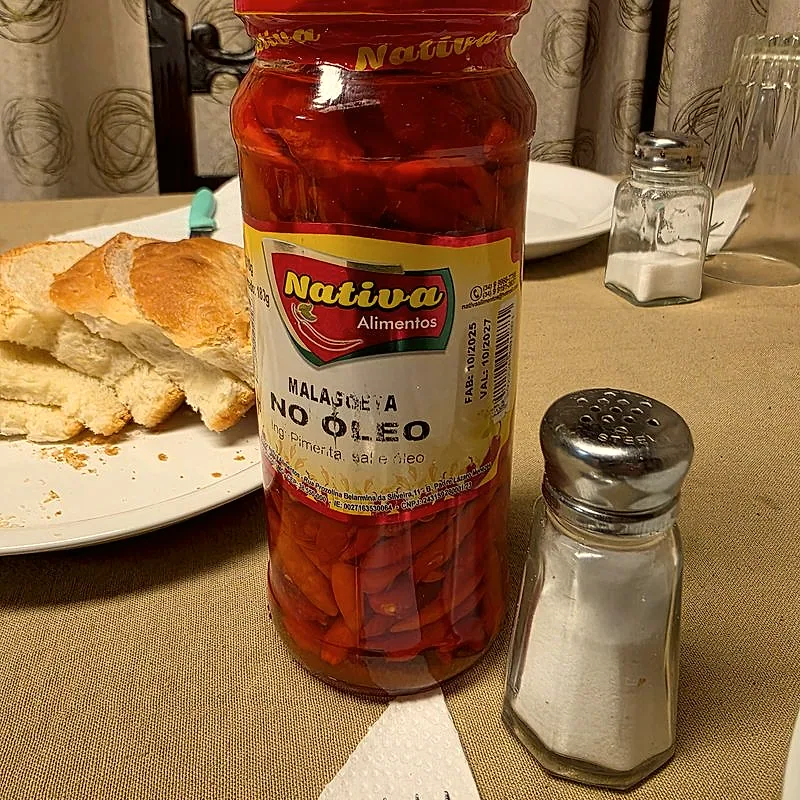 A jar of preserved red malagueta peppers, visible through the glass above and below the label