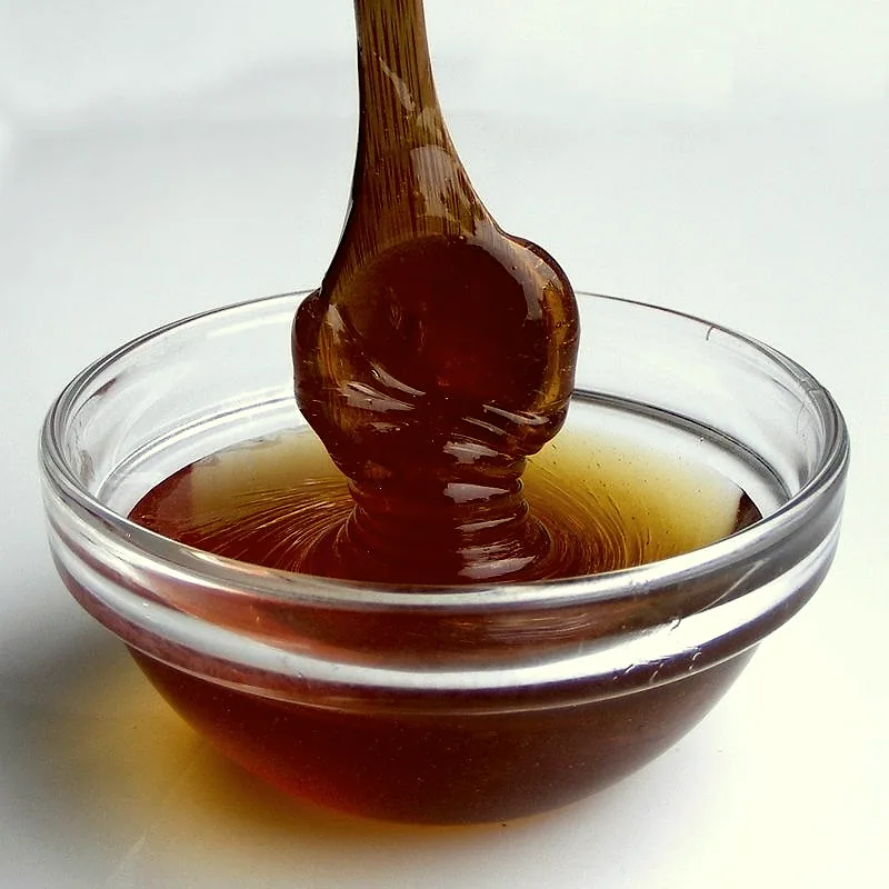 A wooden dipper lifting thick, glossy amber maltose syrup from a glass bowl