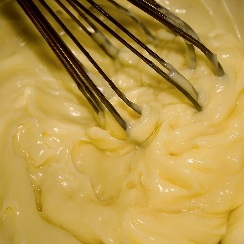 A close-up of thick, pale yellow mayonnaise being whisked in a bowl