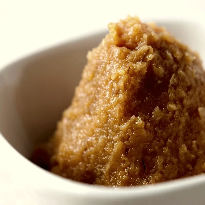 A white bowl of medium-brown miso paste, thick and coarse-textured