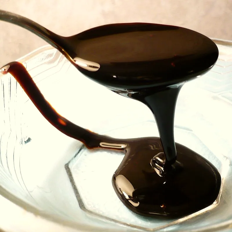 Thick dark molasses dripping from a spoon into a glass bowl