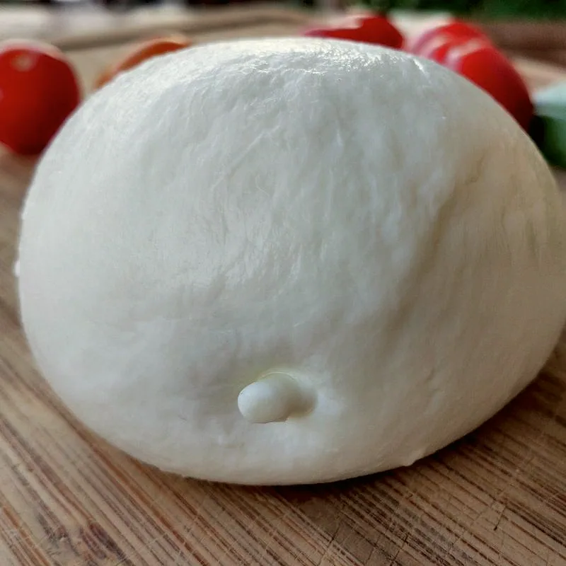 A ball of buffalo mozzarella on a wooden board, its surface faintly creased