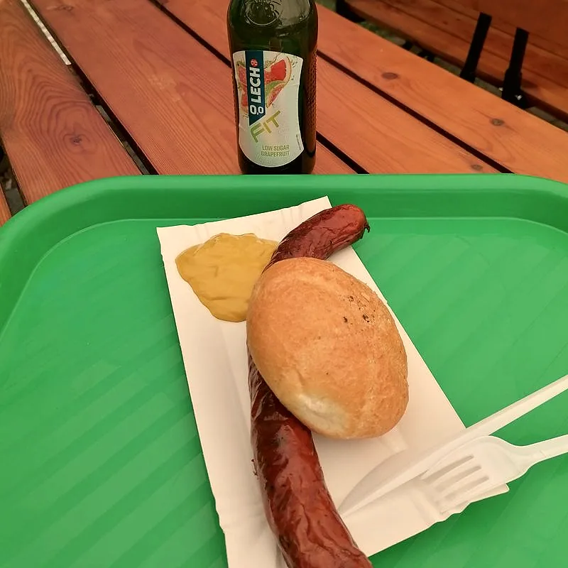 A dollop of yellow prepared mustard on paper, beside a grilled sausage and bread roll