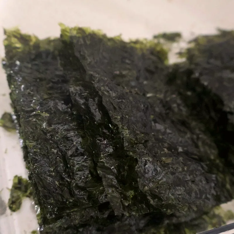 A stack of thin, dark green dried seaweed sheets, glossy and crinkled at the edges