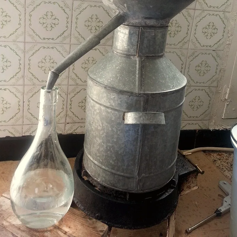 Clear orange blossom water collecting in a glass flask from a traditional copper still