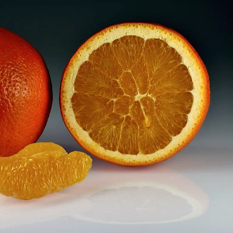 A whole orange beside a halved orange showing its juicy segmented flesh, with a peeled segment in front